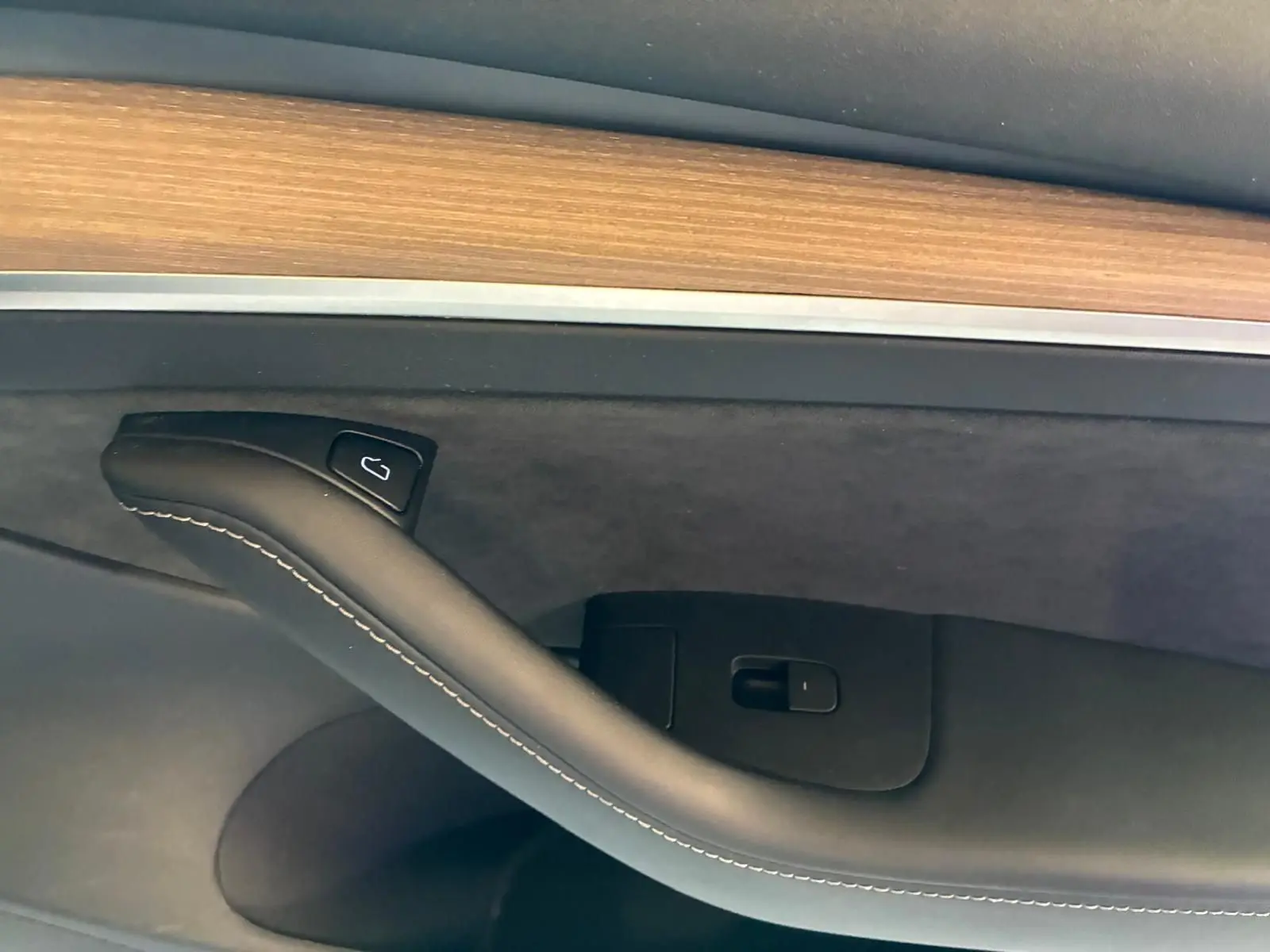 Détail de la poignée intérieure côté gauche d'une Tesla Model 3 blanche 2023 avec insert bois et surpiqûres blanches.