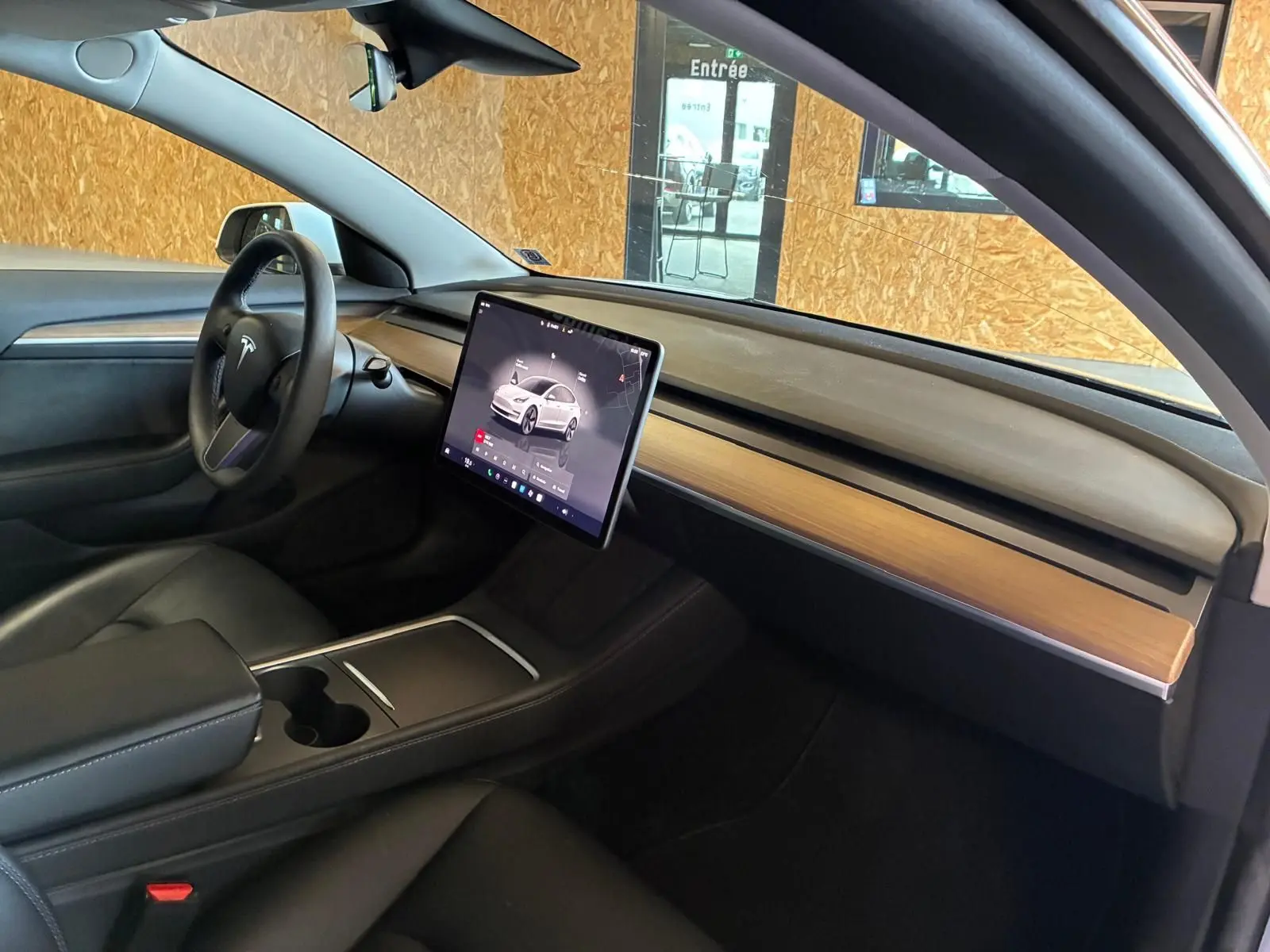 Intérieur de la Tesla Model 3 blanc, vue côté conducteur montrant le tableau de bord épuré avec écran tactile central.