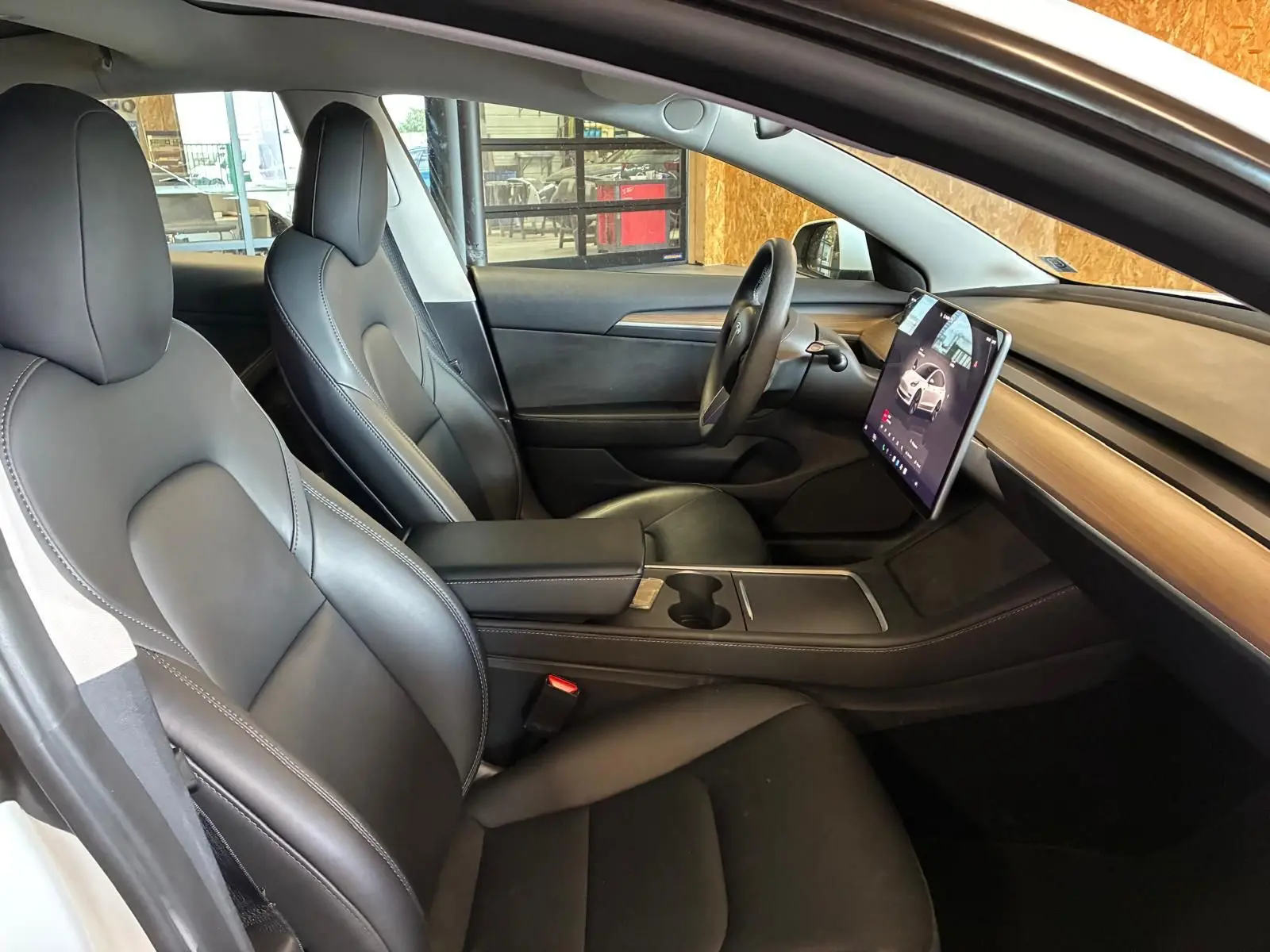 Vue intérieure côté gauche du Tesla Model 3 blanc 2023, mettant en valeur les sièges noirs et l'écran tactile central vertical.