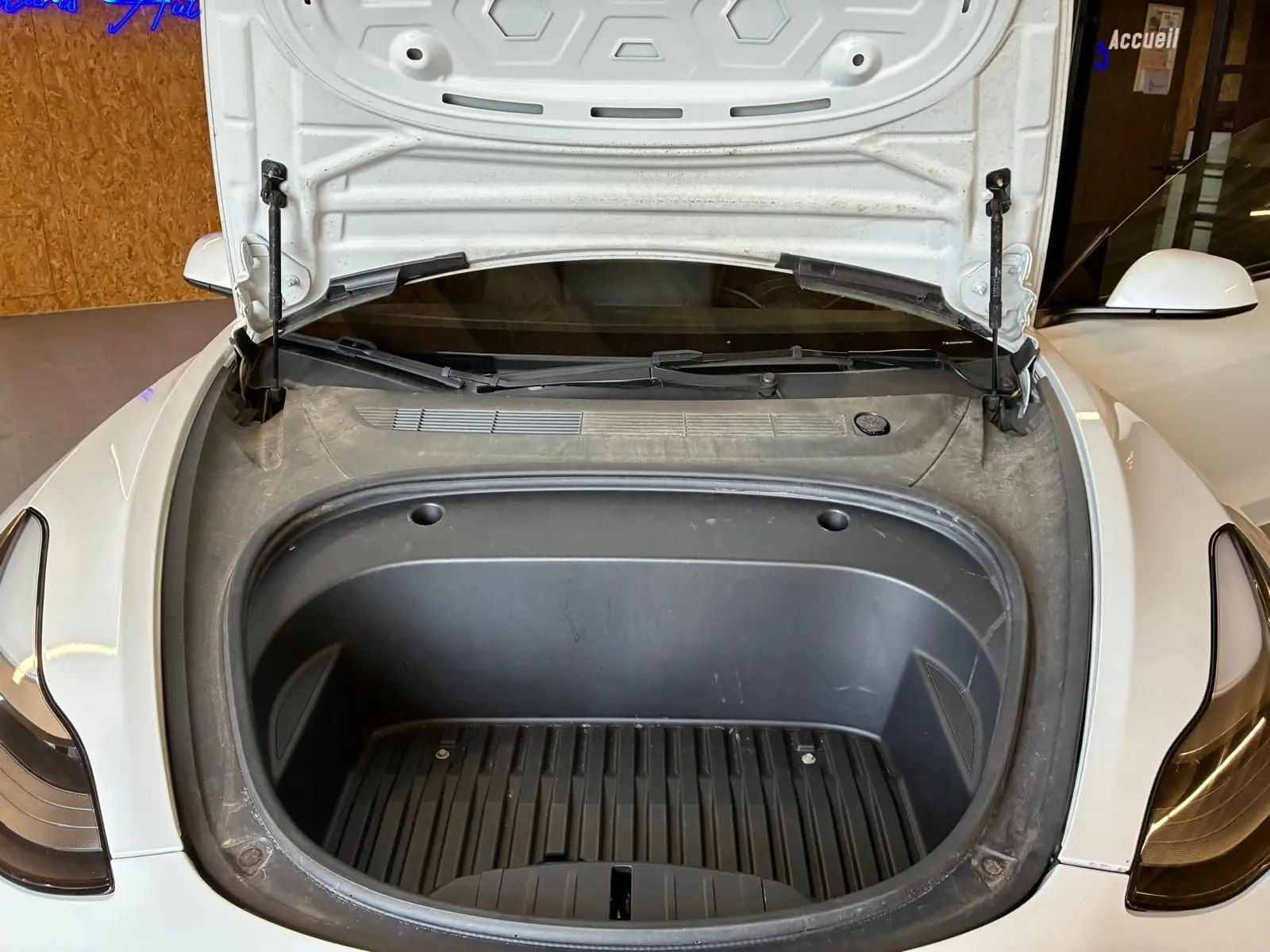 Vue avant rapprochée du coffre avant ouvert d’une Tesla Model 3 blanche, montrant l’espace de rangement électrique.