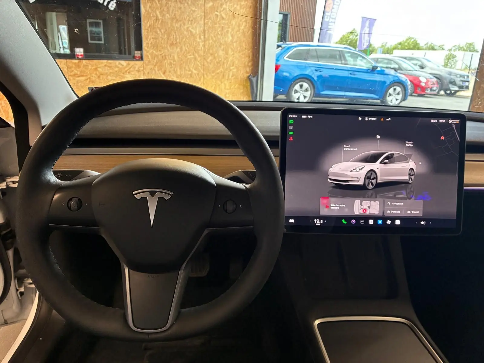 Vue intérieure centrée sur le volant noir et l'écran tactile du tableau de bord d'une Tesla Model 3 blanche de 2023.