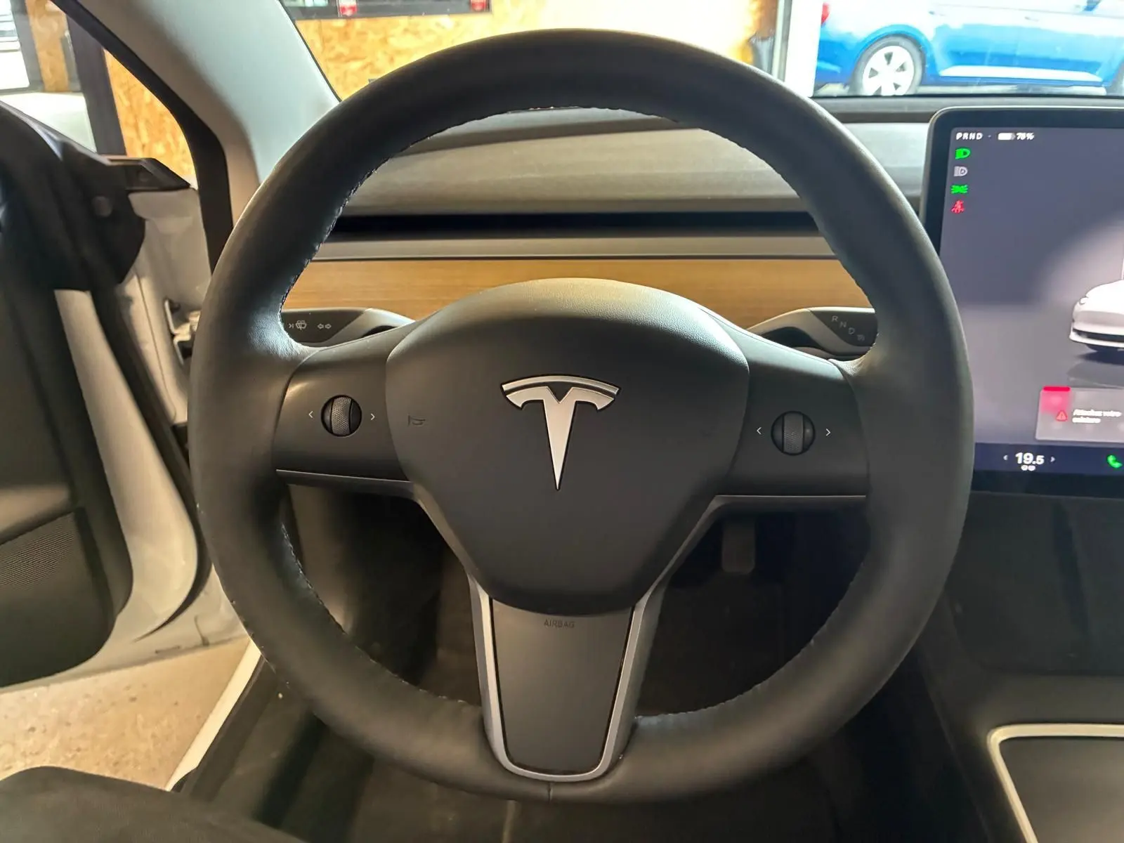 Vue intérieure centrée sur le volant noir d’un Tesla Model 3 blanc 2023, avec écran tactile visible à droite.