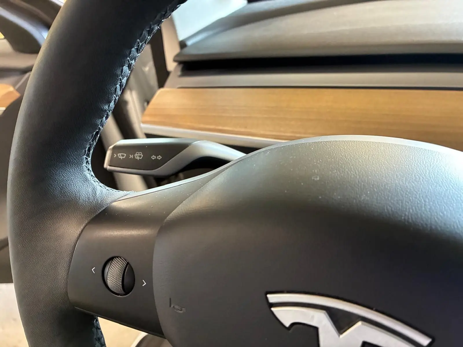 Gros plan sur le volant noir de la Tesla Model 3 blanc, avec commande multifonction et tableau de bord en bois visible.