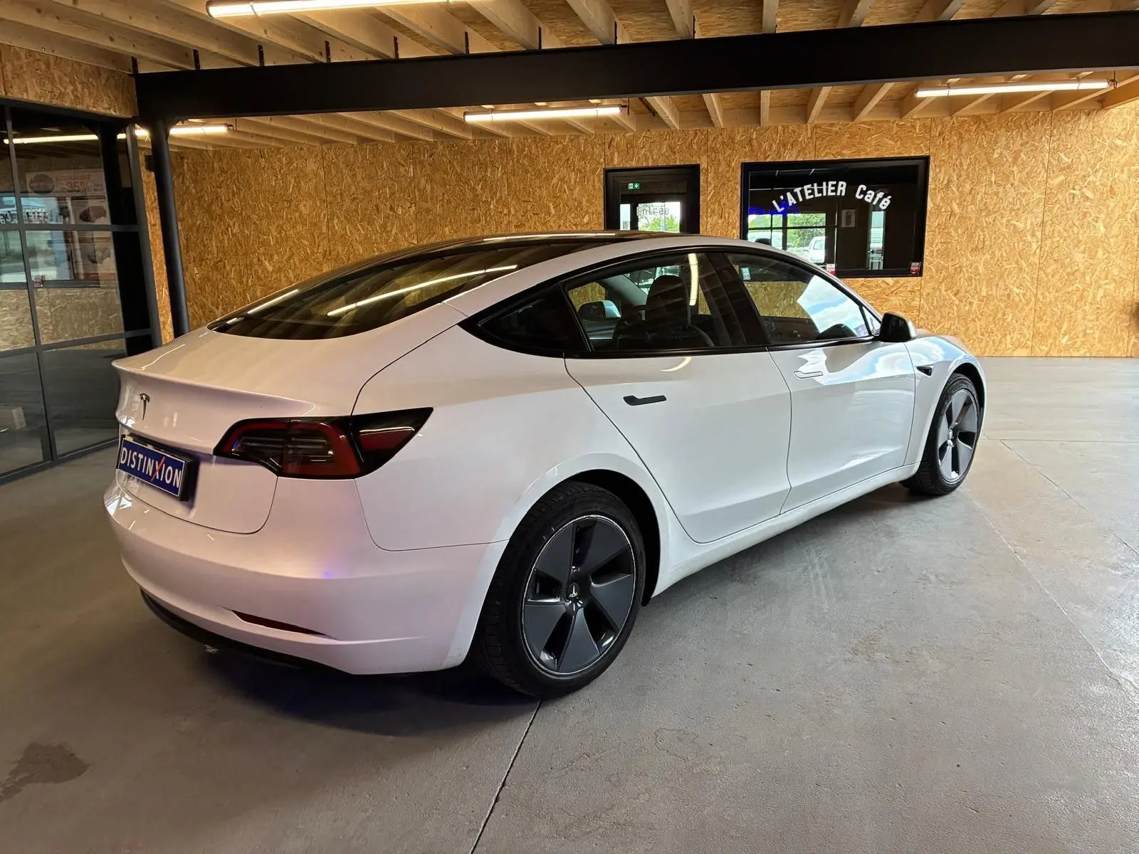 Tesla Model 3 blanc vue 3/4 arrière droit dans un garage avec jantes noires distinctives et toit panoramique.
