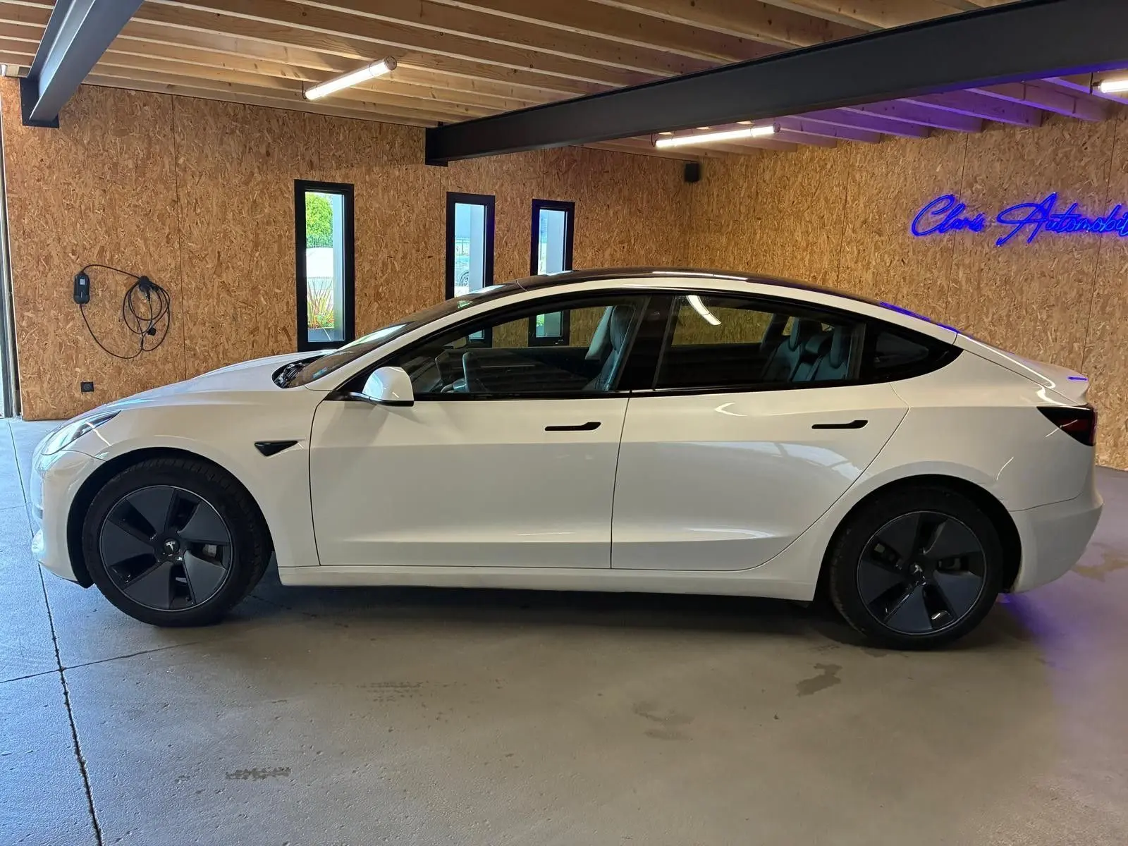 Vue de profil côté gauche d'une Tesla Model 3 blanche 2023, avec jantes noires et poignées affleurantes.