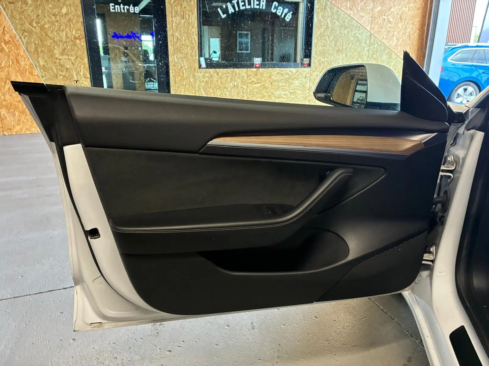 Vue intérieure de la porte côté gauche d’un Tesla Model 3 blanc 2023, avec garniture noire et insert imitation bois.