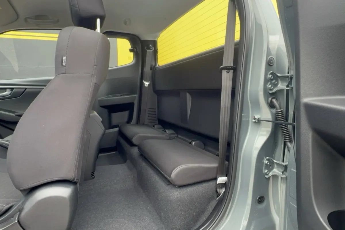 Vue intérieure côté arrière droit du pick-up Isuzu D-MAX 2.2 TD 164 Space Evolution avec banquette arrière rabattue et sellerie tissu noire.