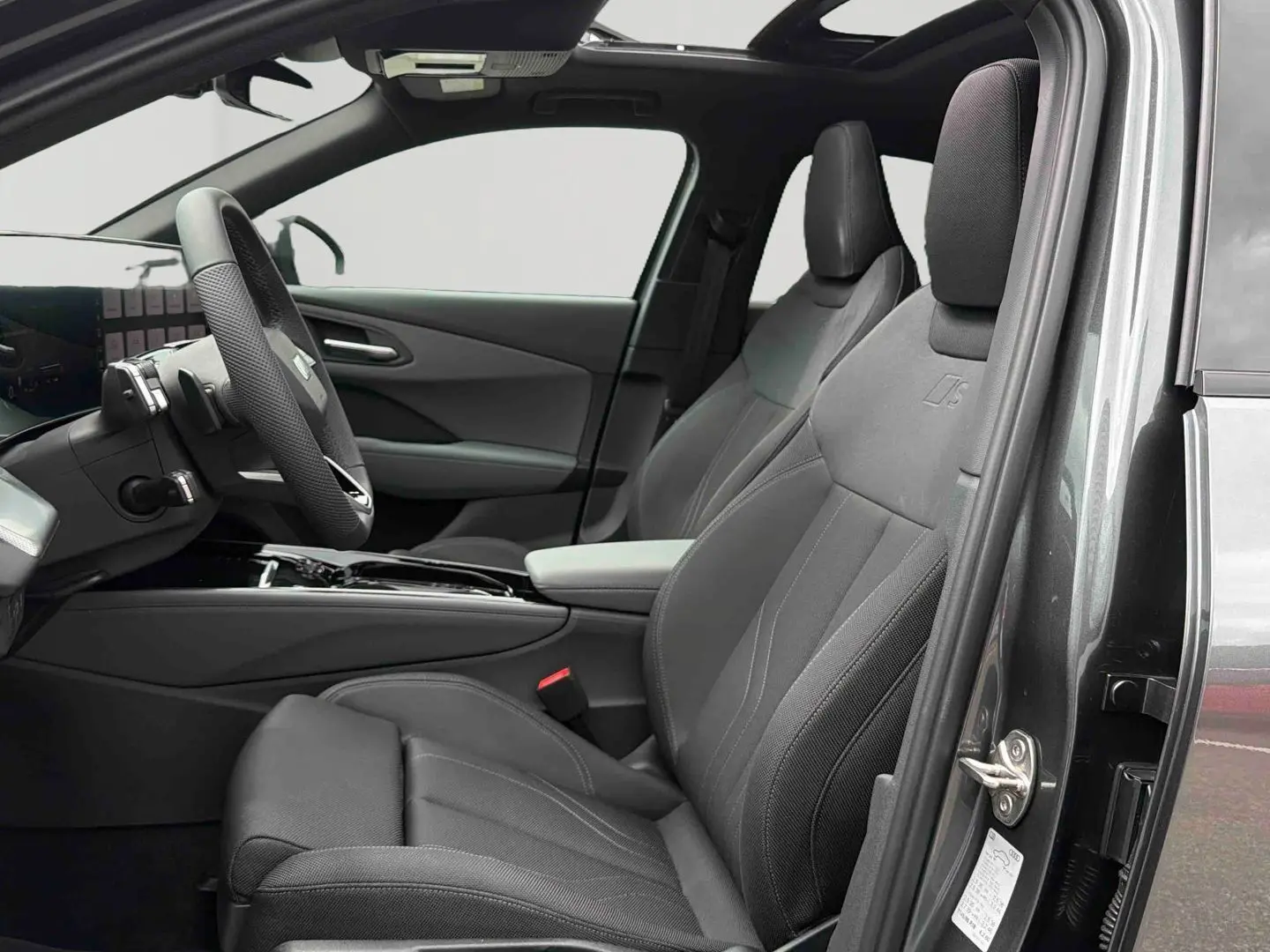 Vue intérieure côté conducteur de l'Audi Q3 Sportback gris, sièges sport avec logo S et toit ouvrant panoramique visible.