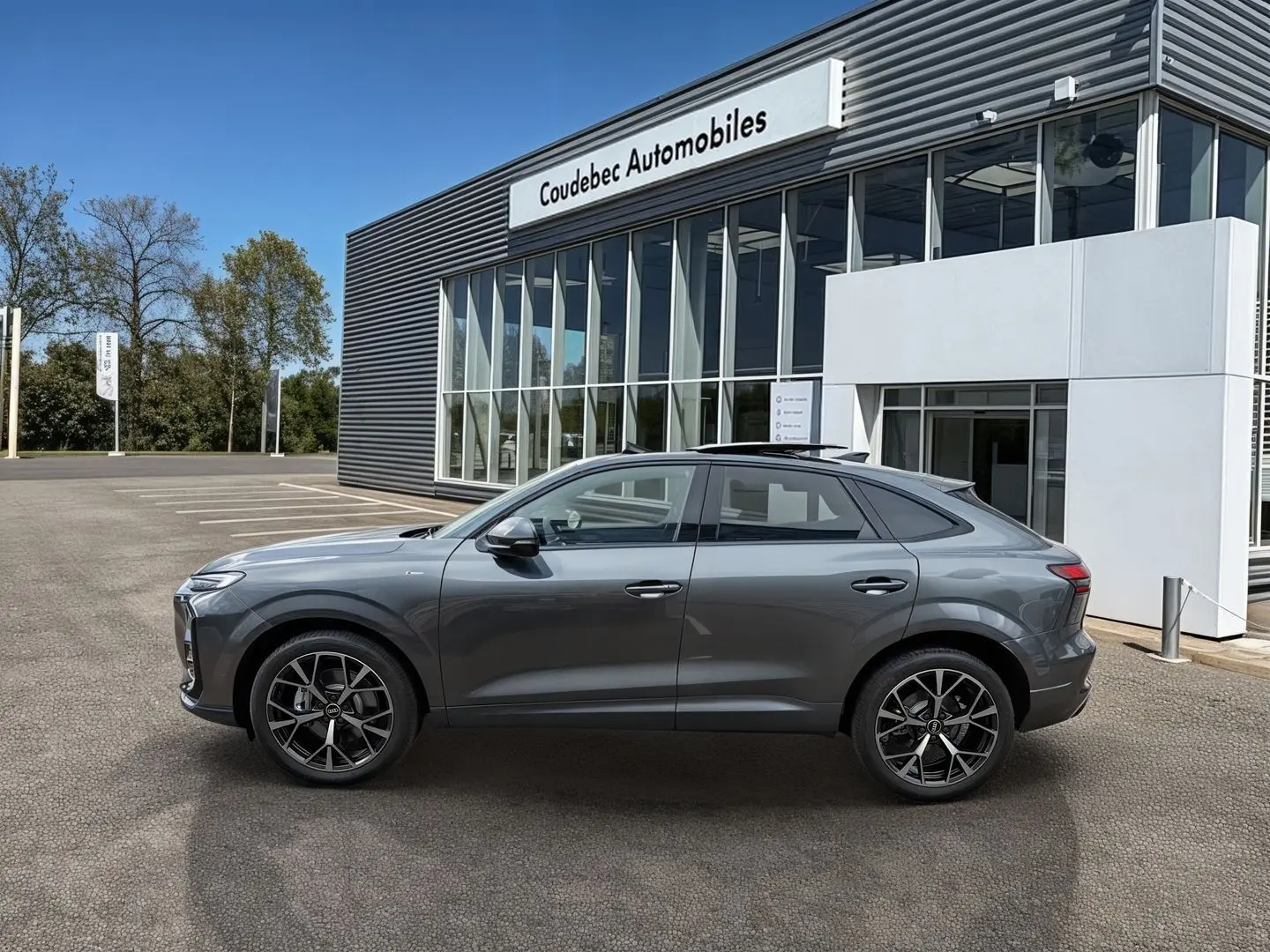 Audi Q3 Sportback gris vue de profil côté gauche, avec jantes noires et toit ouvrant panoramique visible.
