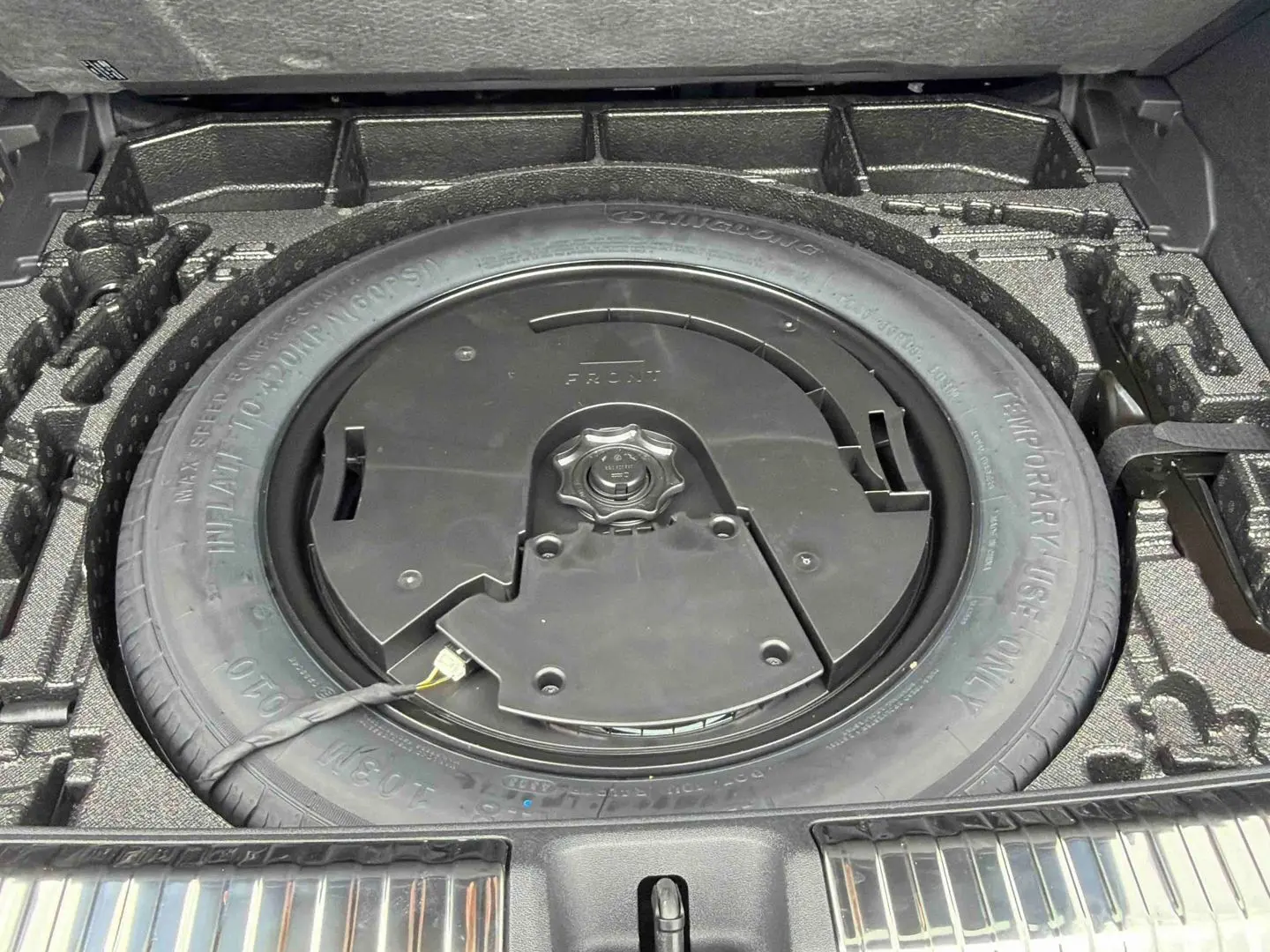 Vue plongeante sur la roue de secours compacte noire dans le coffre de l'Audi Q3 Sportback gris 2026.