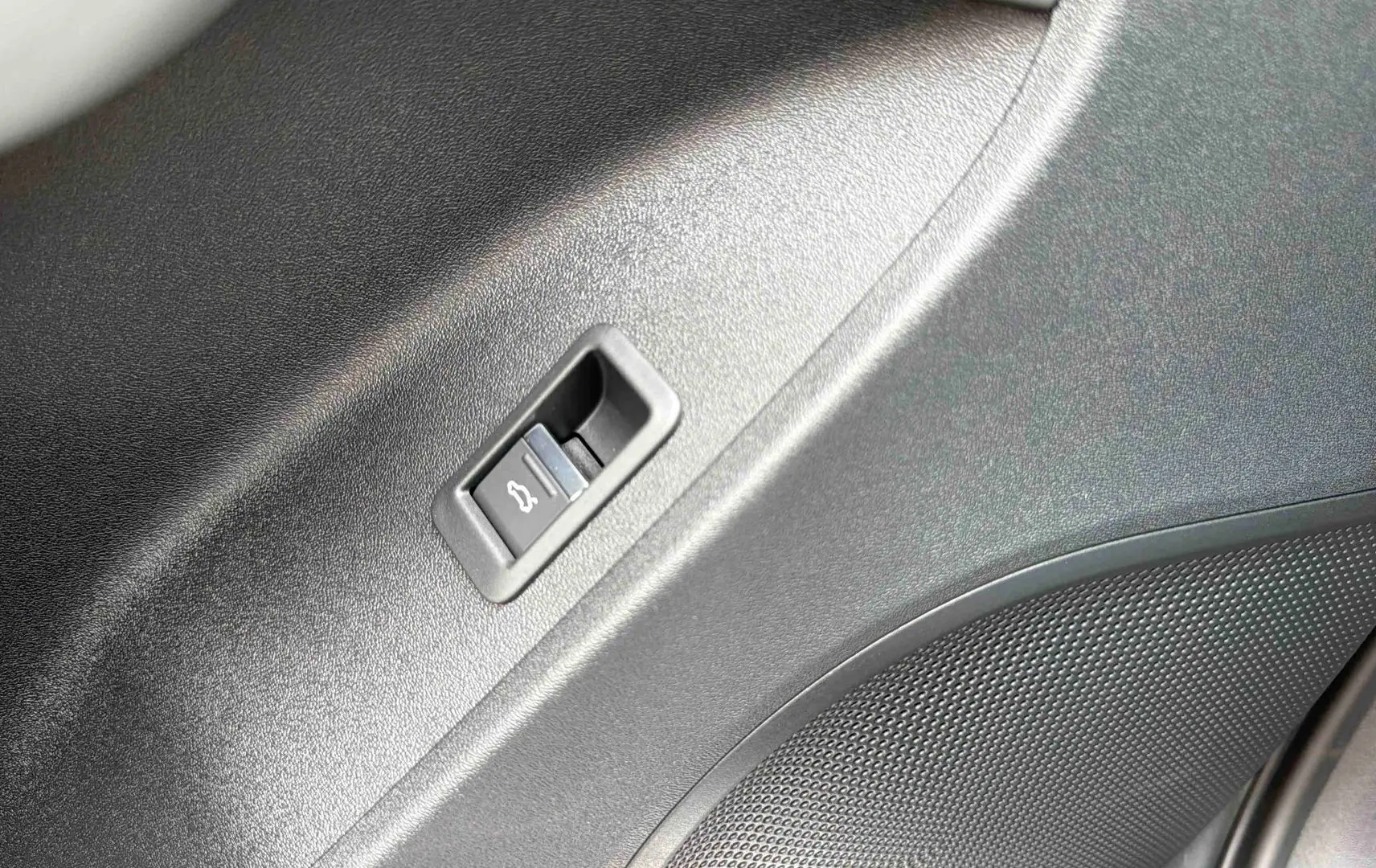 Détail du bouton d'ouverture électrique du hayon sur la garniture intérieure noire du coffre de l'Audi Q3 Sportback gris.