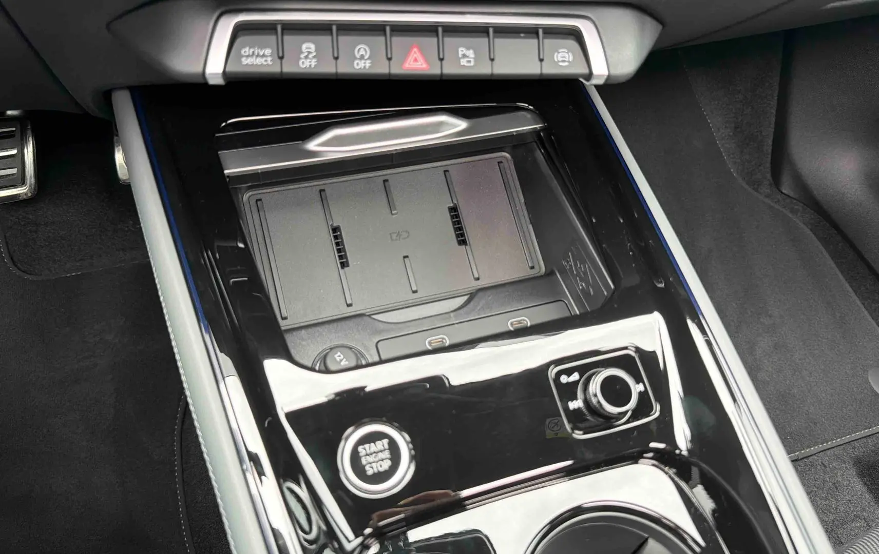 Vue rapprochée de la console centrale noire brillante de l’Audi Q3 Sportback 2026 avec boutons et zone de recharge sans fil.