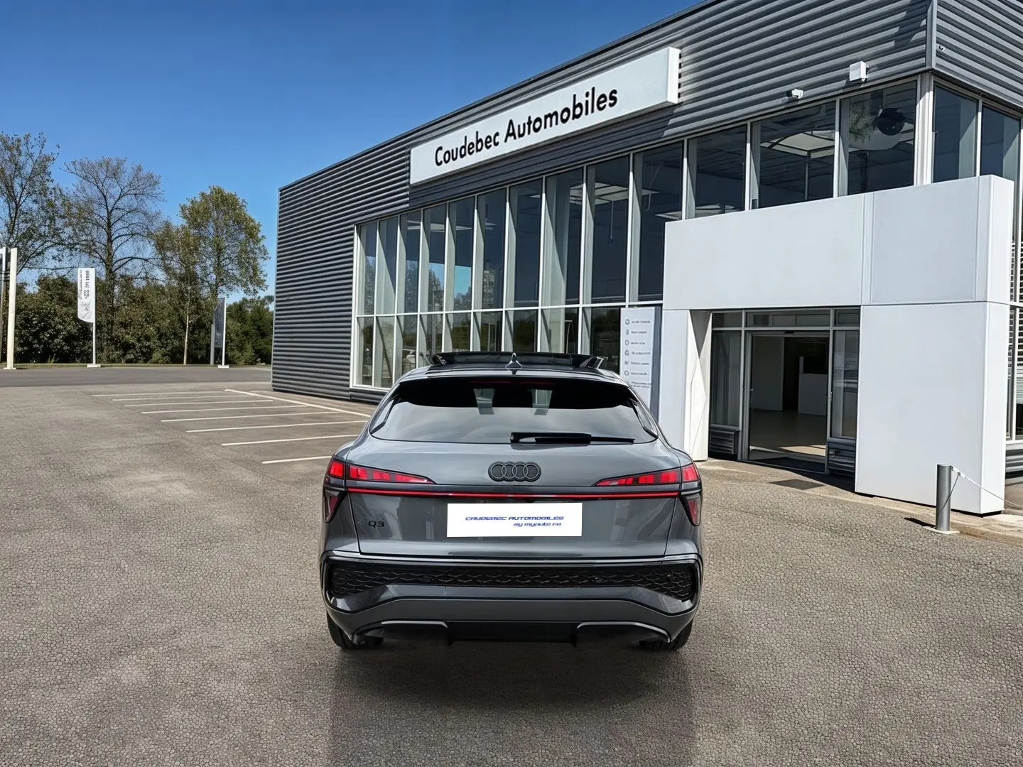 Vue arrière d'un Audi Q3 Sportback gris avec feux LED distinctifs, garé devant un bâtiment moderne.