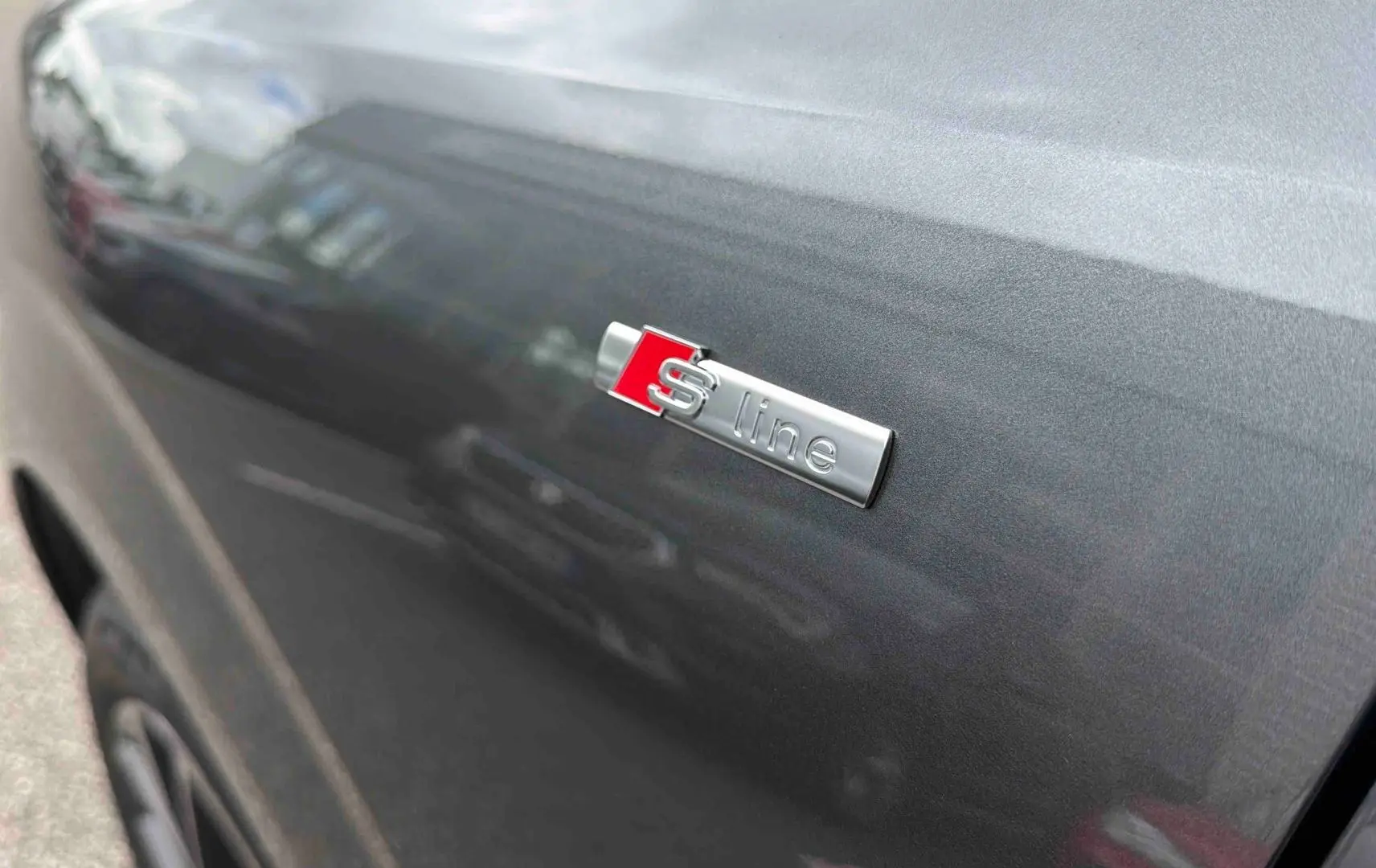 Gros plan sur l'emblème S line sur la porte côté gauche d'un Audi Q3 Sportback gris métallisé.
