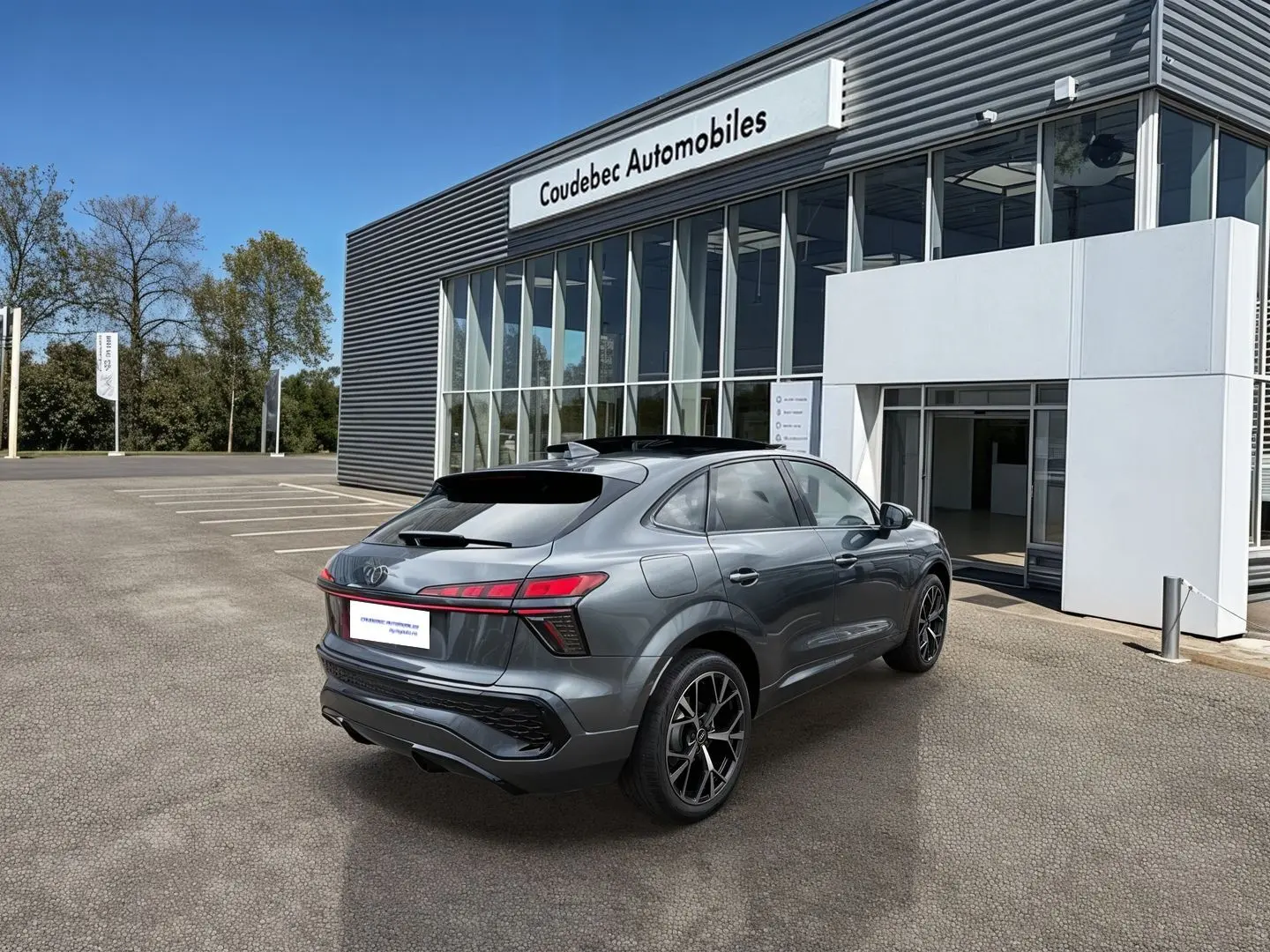 Vue 3/4 arrière droite d'un Audi Q3 Sportback gris métallisé avec jantes noires devant un bâtiment moderne.