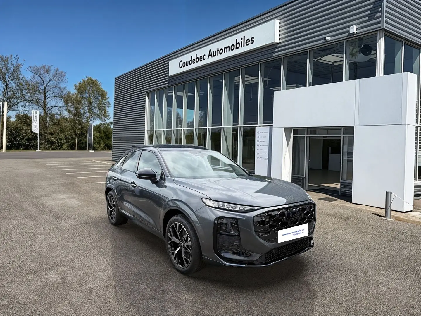 Audi Q3 Sportback gris, vue 3/4 avant droit, avec jantes noires et calandre noire brillante devant un showroom.