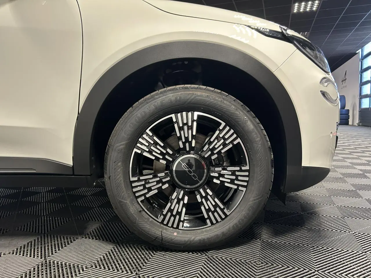 Gros plan sur la roue avant droite noire et chrome d'une FIAT 600 blanche, avec partie avant du véhicule visible.