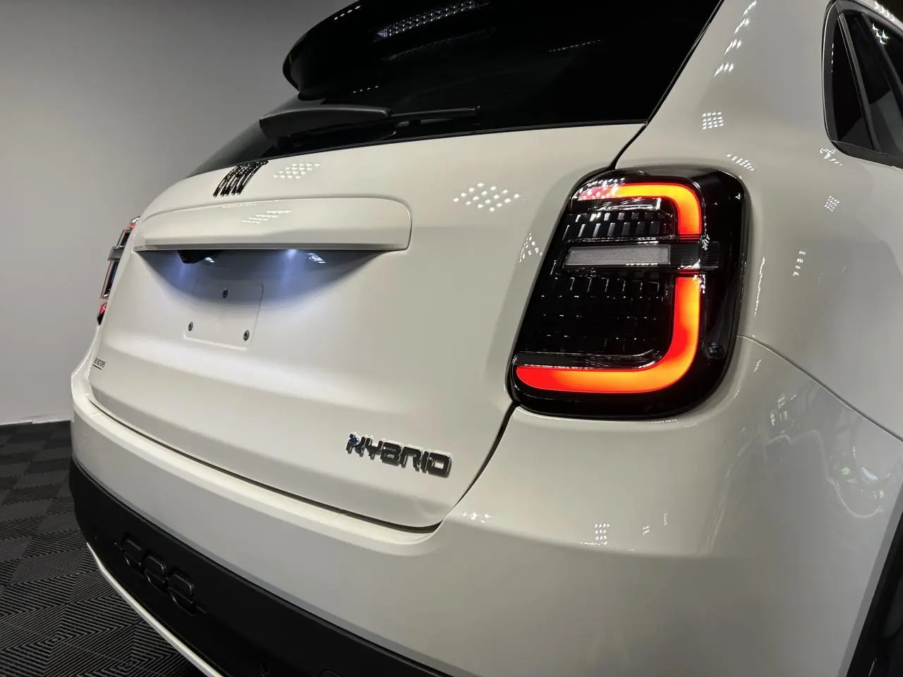 Vue arrière droite d'une FIAT 600 blanche hybride avec feux arrière LED allumés et logo Hybrid sur le hayon.