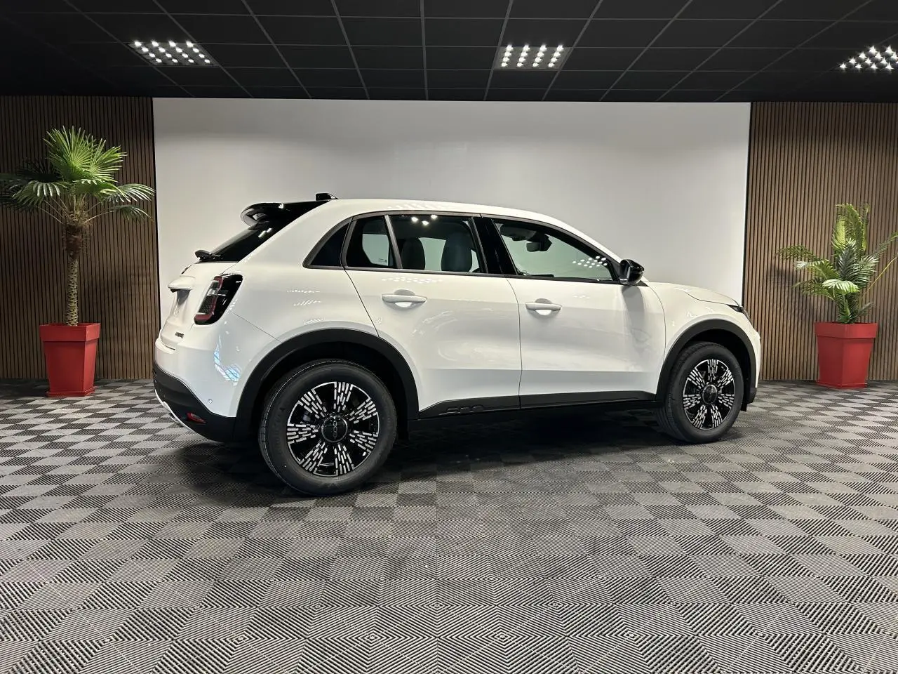 Vue latérale droite d'un FIAT 600 blanc avec jantes alliage noires et toit noir dans un showroom.