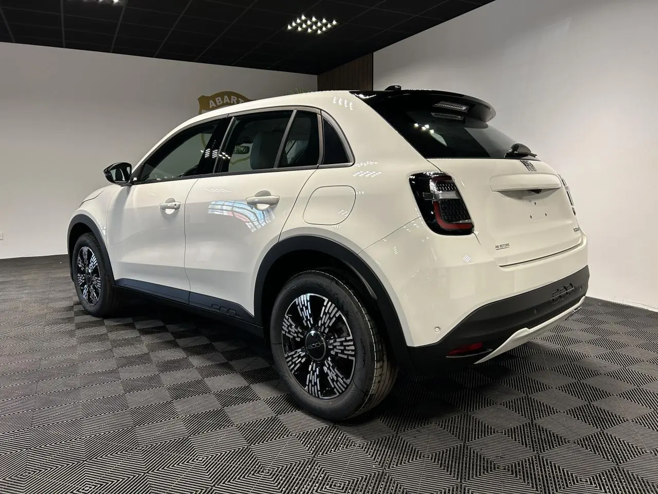 Vue 3/4 arrière droite d'un FIAT 600 blanc avec jantes noires et toit noir brillant dans un showroom.
