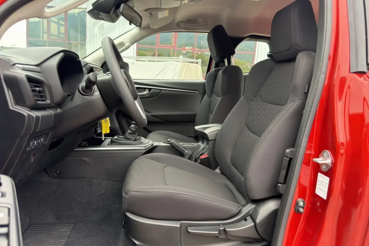 Vue intérieure côté conducteur du pick-up Isuzu D-MAX 2.2 TD 164 avec sièges tissu noirs et porte ouverte rouge.