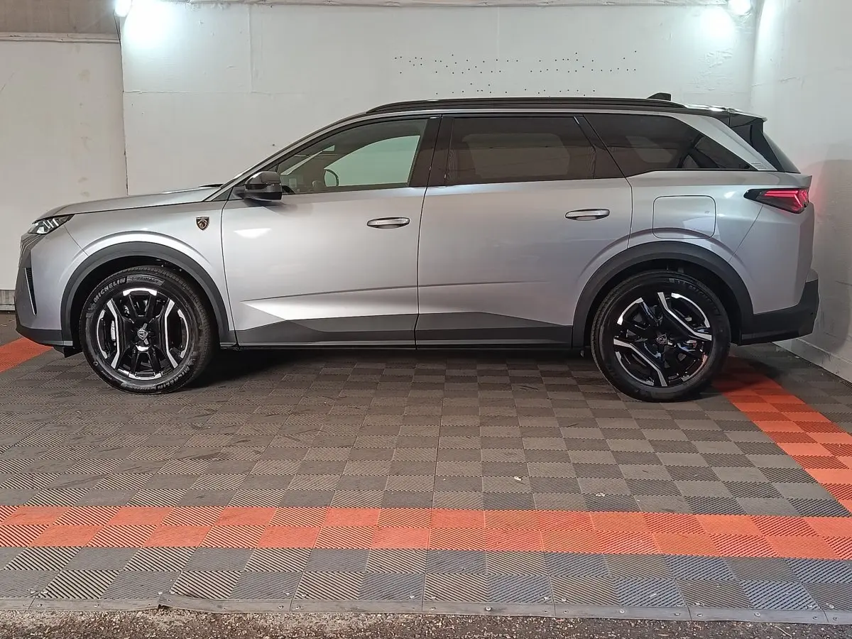 Vue latérale droite d’un Peugeot 5008 gris clair avec jantes noires et toit noir en intérieur fermé.