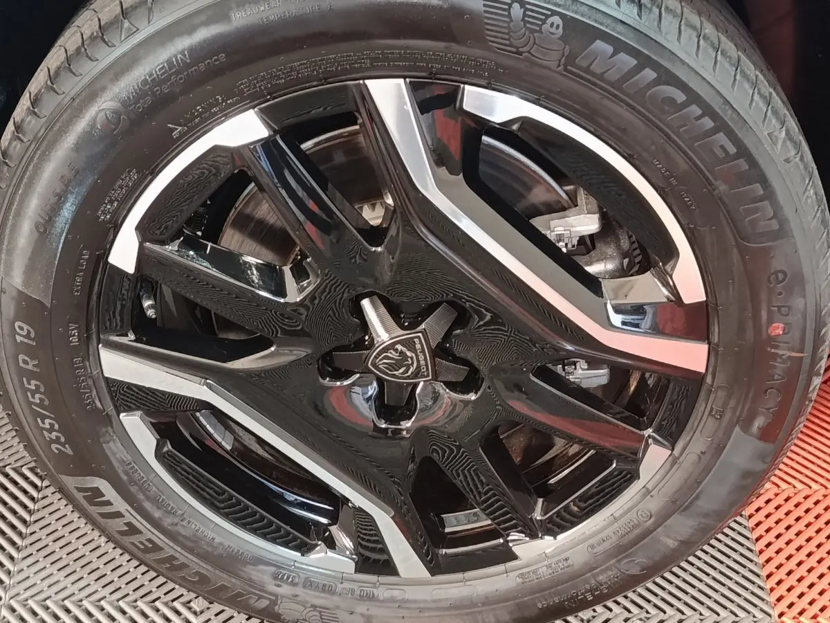 Gros plan sur la roue avant droite du Peugeot 5008 gris clair, jante alliage noire et argentée avec logo lion central.