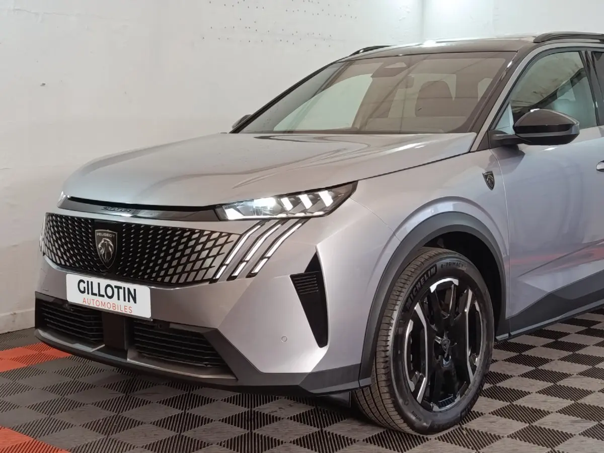 Vue 3/4 avant droite d'un Peugeot 5008 gris clair avec calandre noire et phares LED distinctifs.