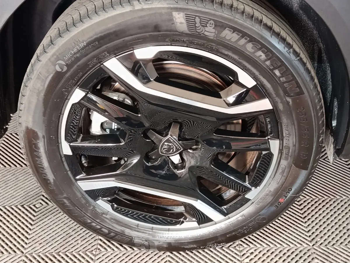 Gros plan sur la jante noire et argentée avec logo Peugeot, montée d’un pneu Michelin sur Peugeot 5008 gris clair.