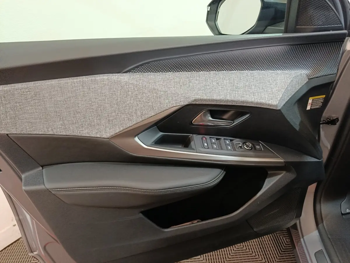 Vue intérieure côté gauche de la porte avant d’un Peugeot 5008 gris clair, avec garniture tissu et commandes électriques.