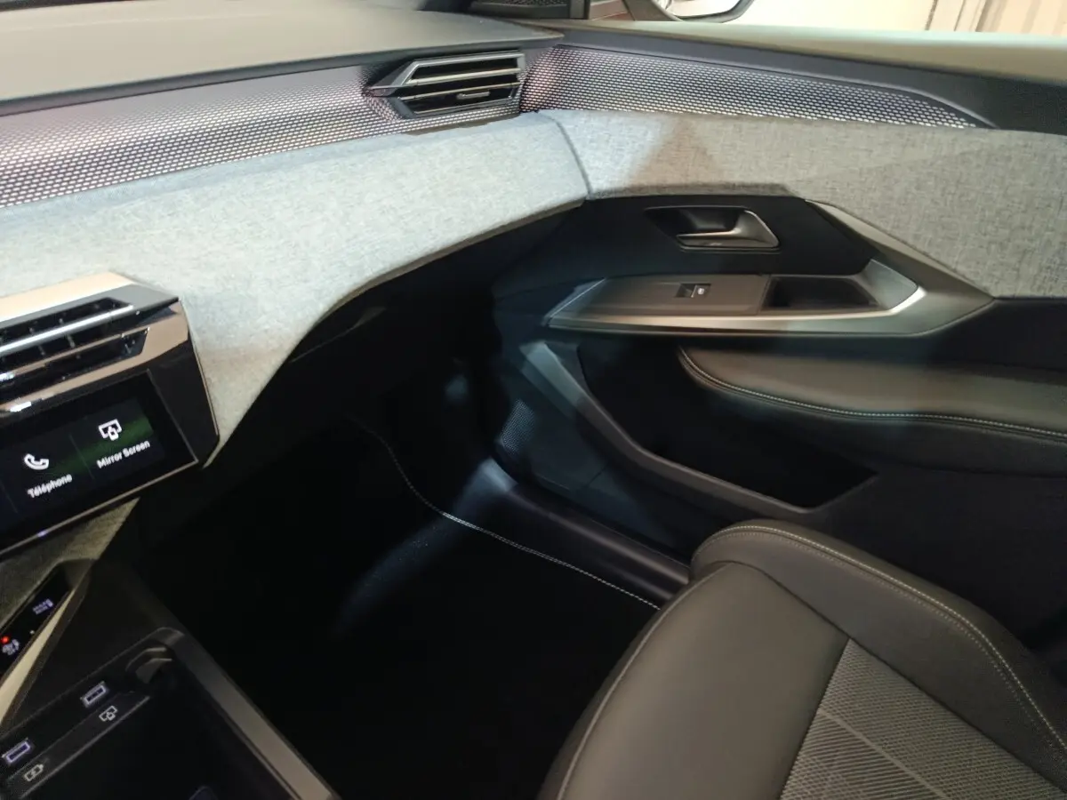 Vue intérieure côté passager du Peugeot 5008 1.6 PHEV 195 E-DCS7 GT 2026 avec tableau de bord gris clair et sièges noirs.