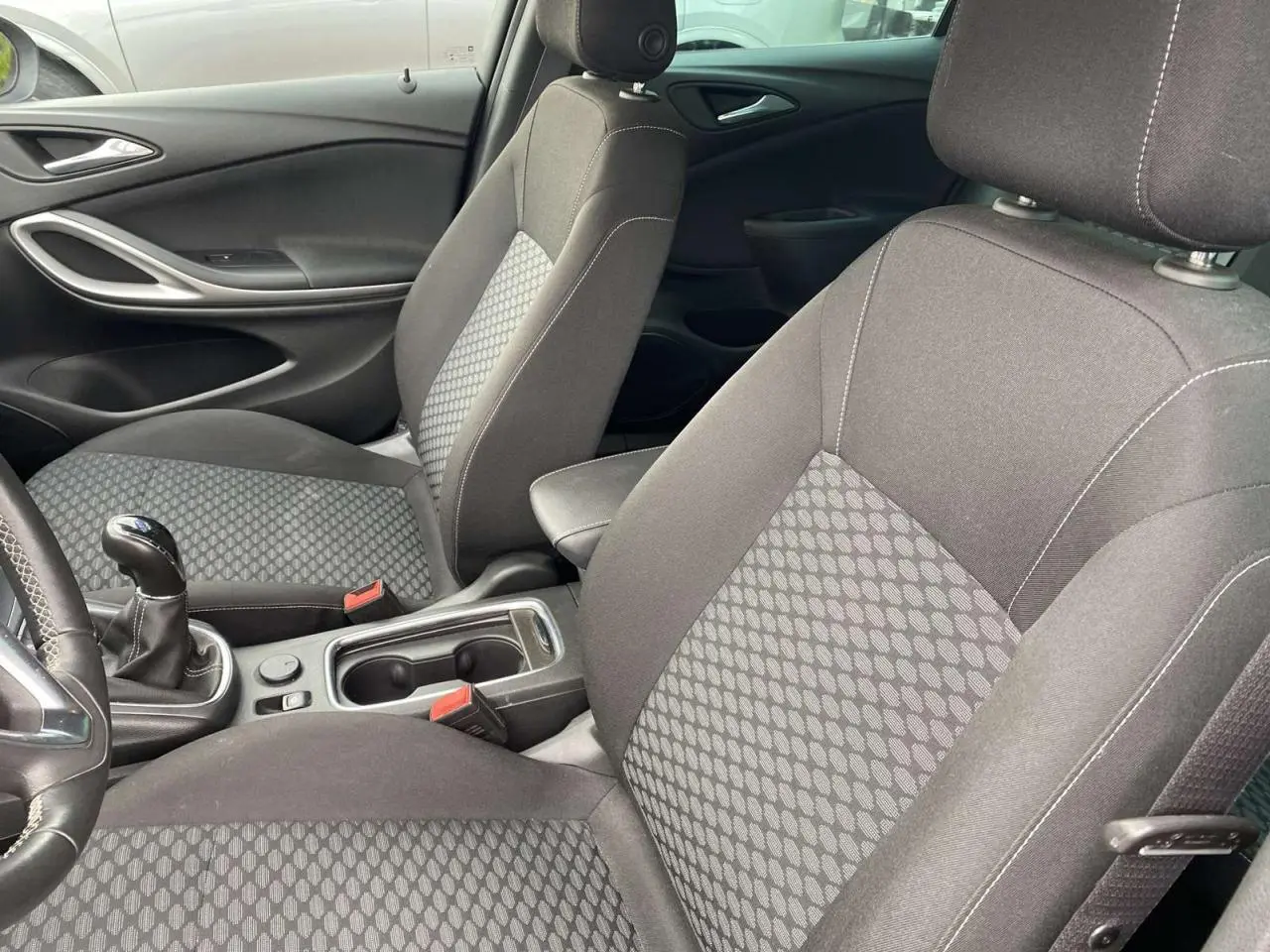 Intérieur avant de l'Opel Astra 2021 avec sièges tissu gris à motifs, levier de vitesse manuel et accoudoir central.