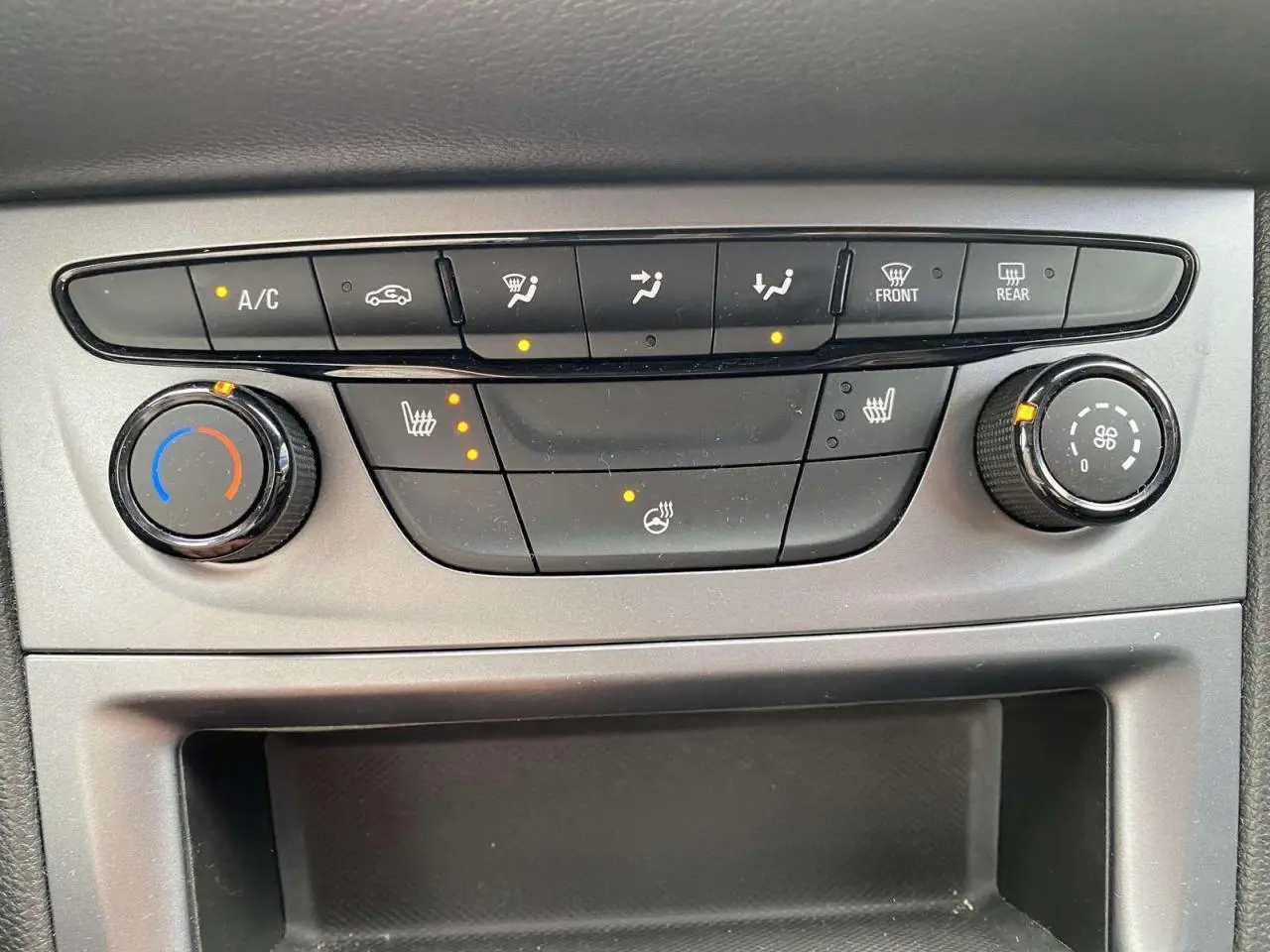 Gros plan sur la console centrale grise de l'Opel Astra 2021, avec commandes de climatisation et sièges chauffants allumés.