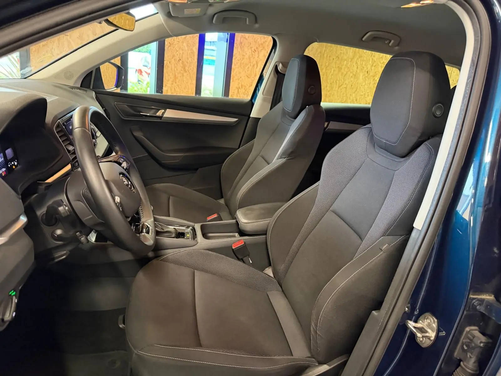 Vue intérieure côté conducteur du Skoda Karoq bleu 2023, montrant les sièges avant noirs et le volant multifonctions.