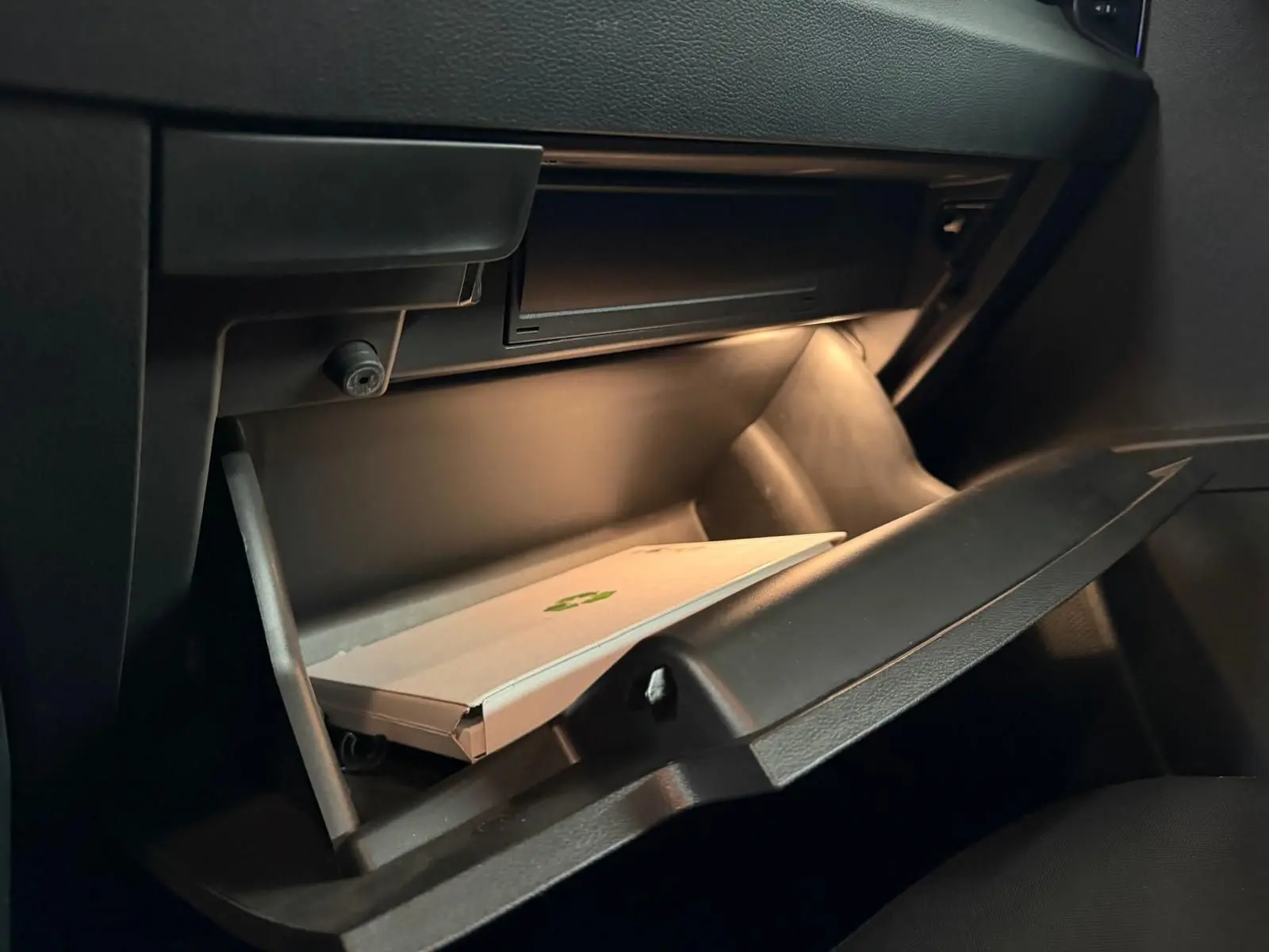 Gros plan sur la boîte à gants ouverte de la Skoda Karoq 2.0 TDI bleu, avec éclairage intérieur et document à l'intérieur.