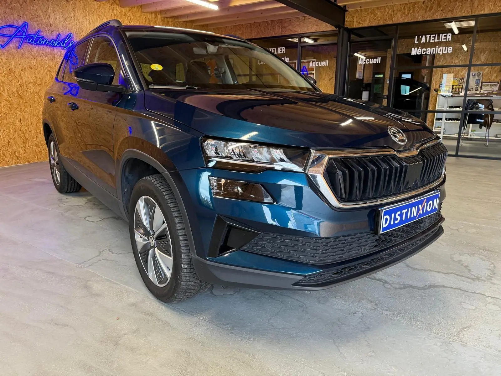Vue 3/4 avant droite d'un Skoda Karoq bleu métallisé avec calandre noire et jantes alu 17 pouces dans un showroom.