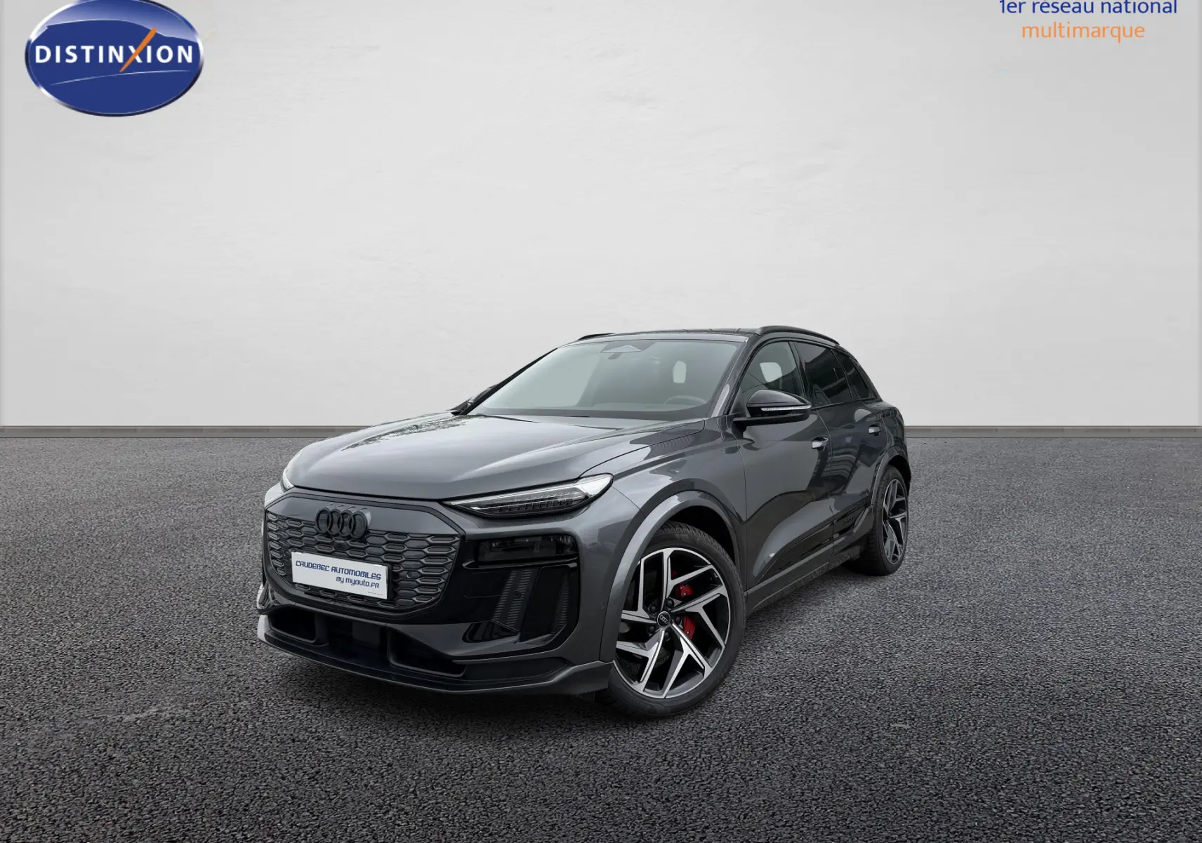 Audi Q6 e-tron gris nacré en 3/4 avant droit, avec jantes sport noires et étriers de frein rouges visibles.