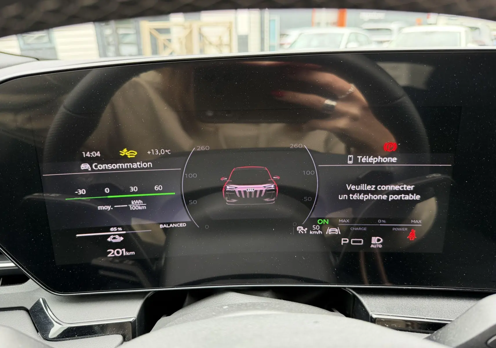 Vue du tableau de bord numérique de l'Audi Q6 e-tron avec affichage de consommation et alertes, volant en arrière-plan.