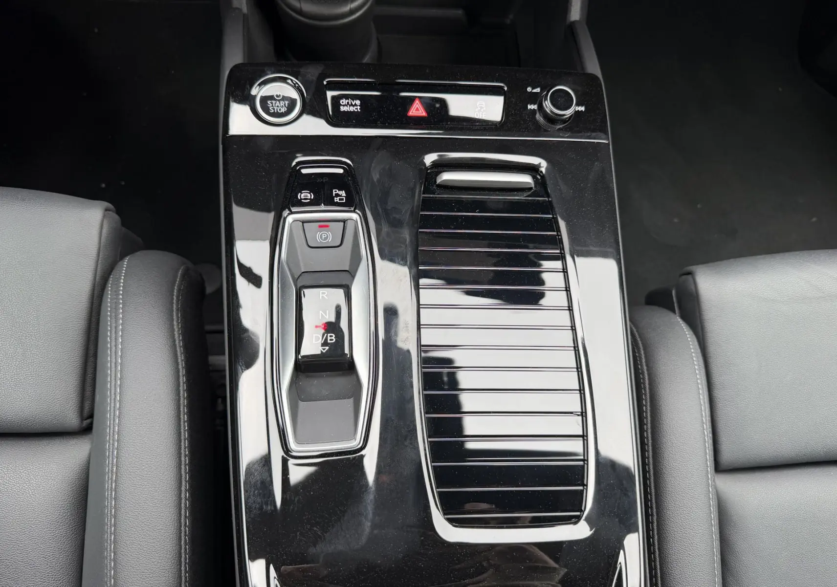 Vue plongeante sur la console centrale noire brillante de l'Audi Q6 e-tron 2024 avec levier de vitesses et boutons de contrôle.
