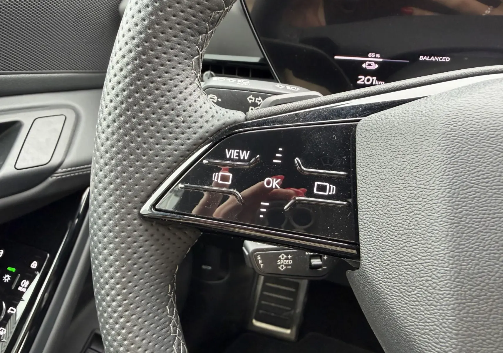 Gros plan sur le volant perforé noir avec commandes tactiles et tableau de bord numérique de l'Audi Q6 e-tron gris.