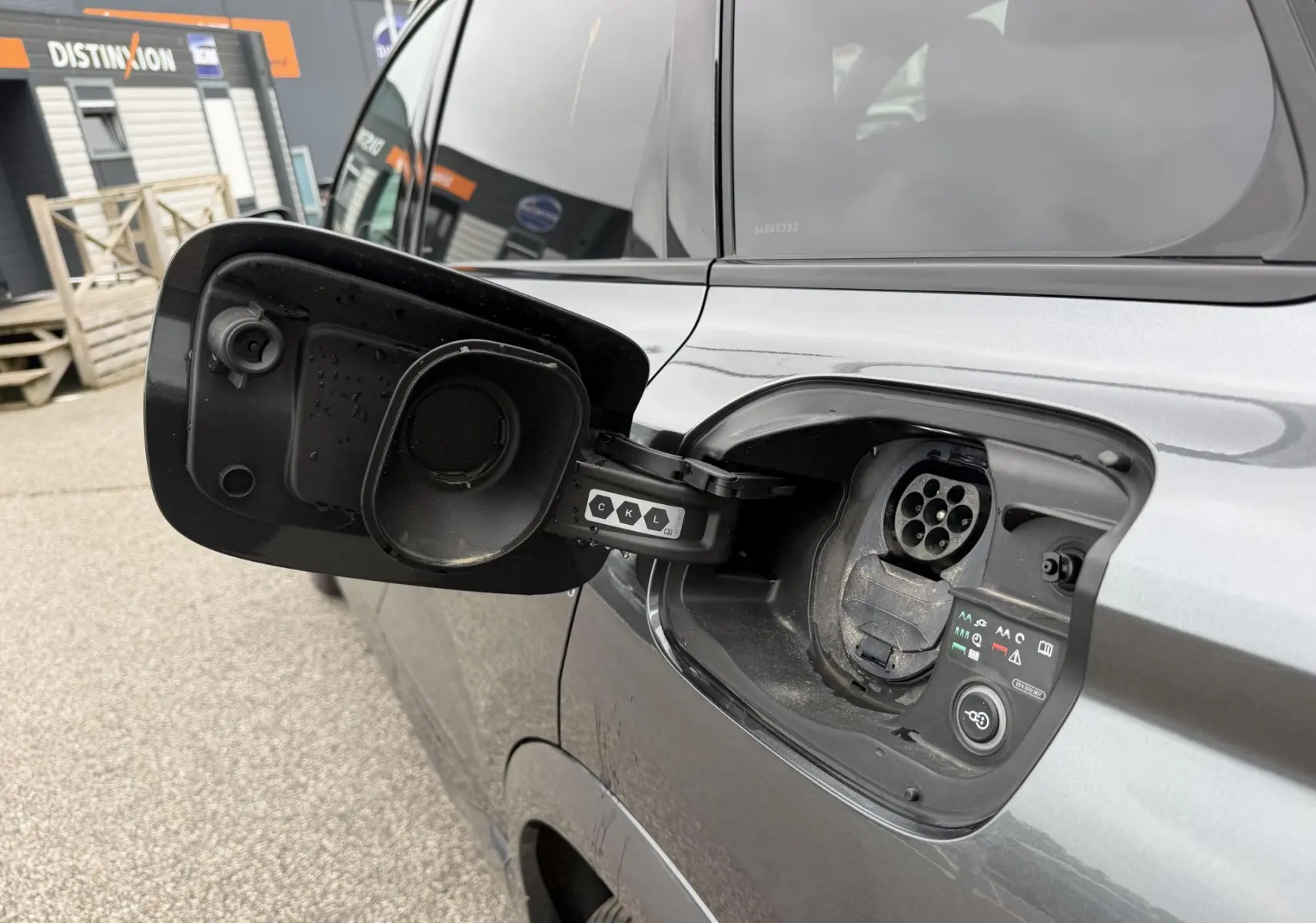 Prise de recharge ouverte côté gauche d’un Audi Q6 e-tron gris nacré, vue rapprochée sur la trappe électrique.