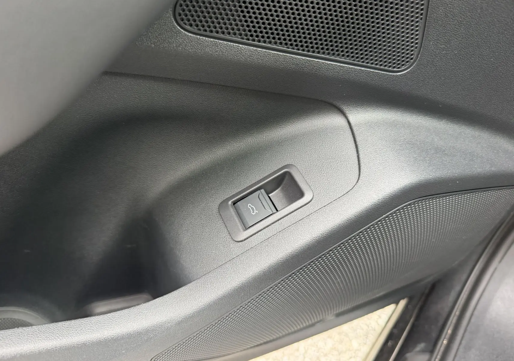 Gros plan sur le bouton d'ouverture du coffre intégré dans la garniture noire de la porte avant droite de l'Audi Q6 e-tron.