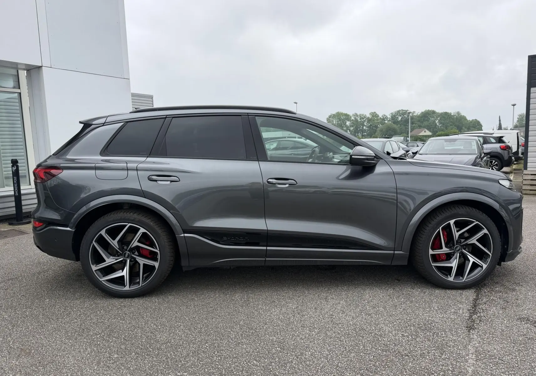 Vue de profil côté gauche d'un Audi Q6 e-tron gris nacré avec jantes sport noires et étriers de frein rouges.