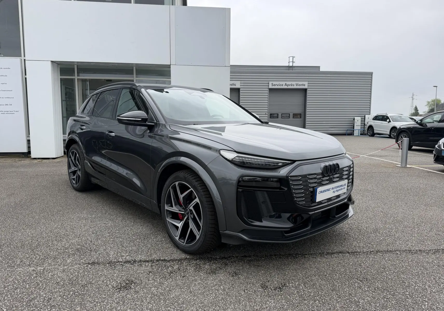 Audi Q6 e-tron gris nacré en 3/4 avant droit, avec jantes noires à cinq branches et étriers de frein rouges.