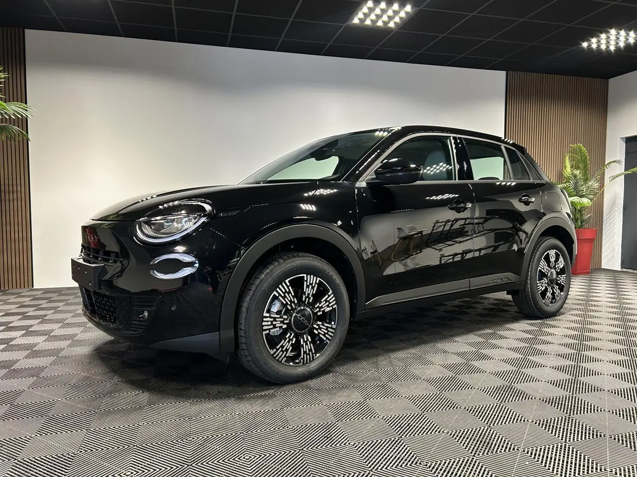 Vue 3/4 avant droite d'une FIAT 600 noire avec jantes alliage noires et détails chromés en intérieur showroom.