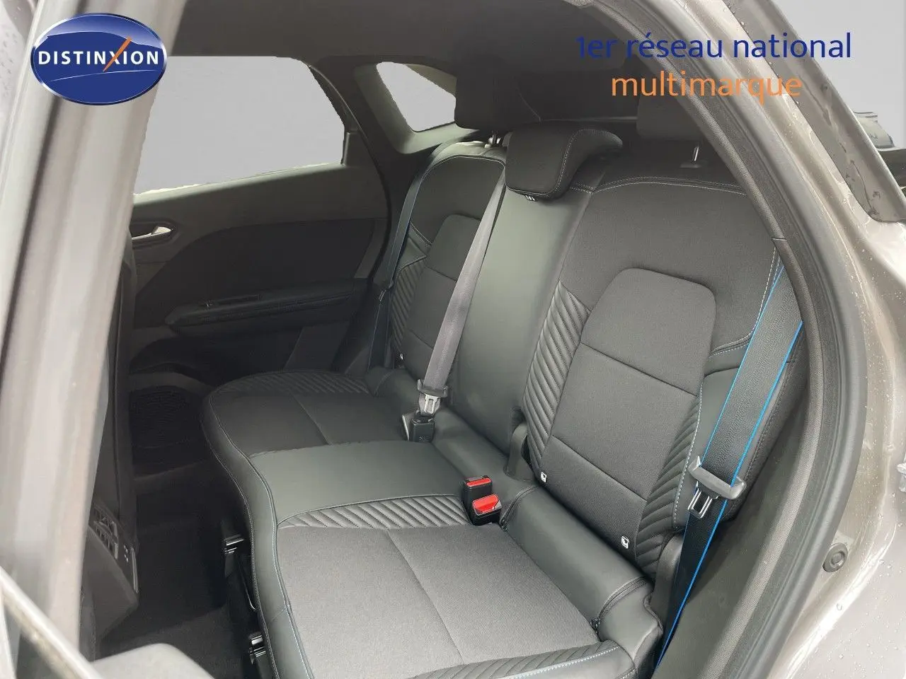Vue intérieure sur la banquette arrière de la Renault Symbioz 2026 gris Cassiopée Métal avec surpiqûres bleues et ceintures assorties.