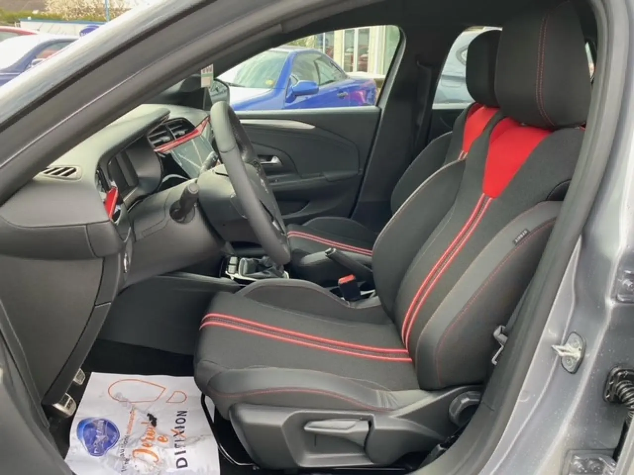 Vue intérieure côté conducteur de l'Opel Corsa gris magnetic 2022 avec sièges tissu noir et rouge et tableau de bord moderne.