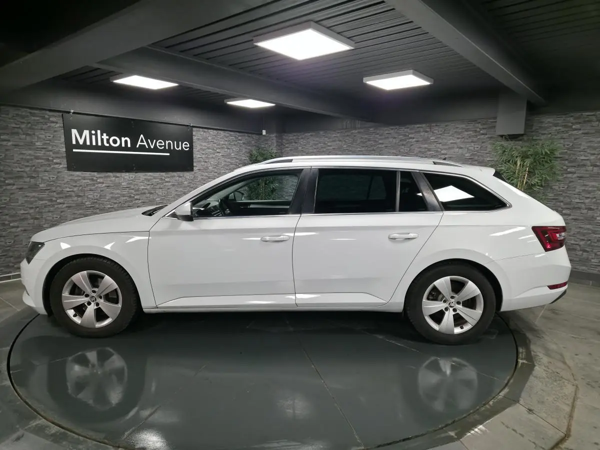Vue de profil côté gauche d'un break SKODA SUPERB blanc avec jantes alliage 17 pouces dans un showroom.