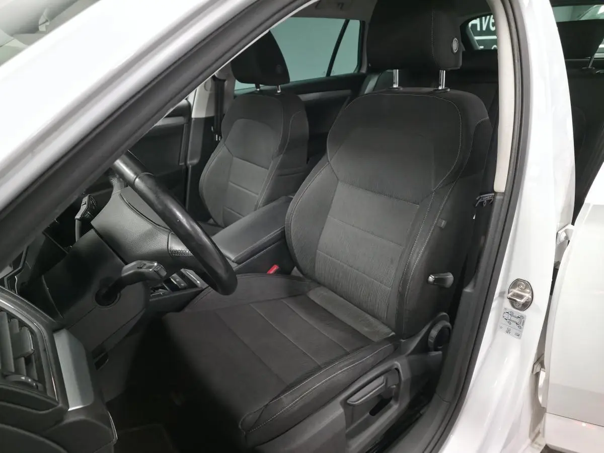 Vue intérieure côté conducteur de la Skoda Superb Combi blanche, sièges tissu noir et volant multifonctions en cuir.