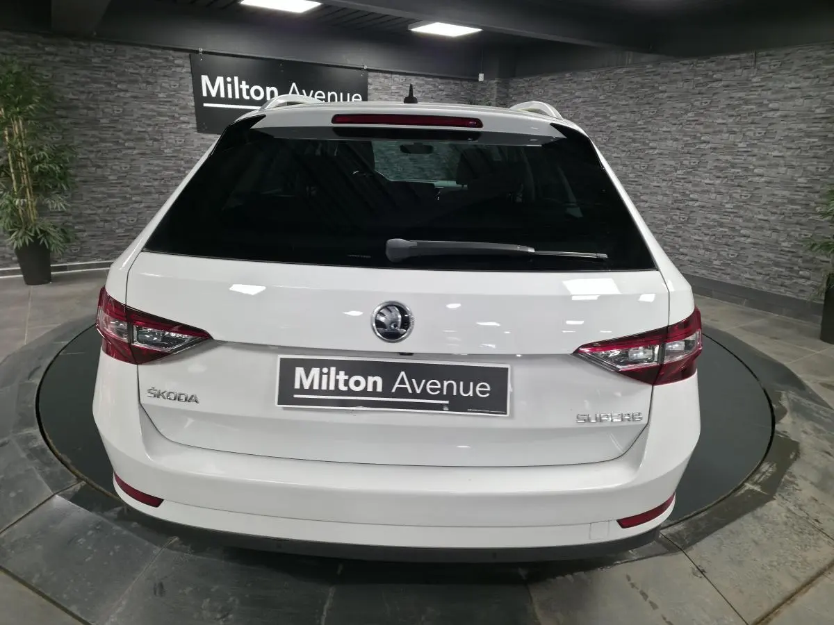Vue arrière d'un break SKODA SUPERB blanc, avec feux arrière LED et logo ŠKODA visible sur un plateau tournant.